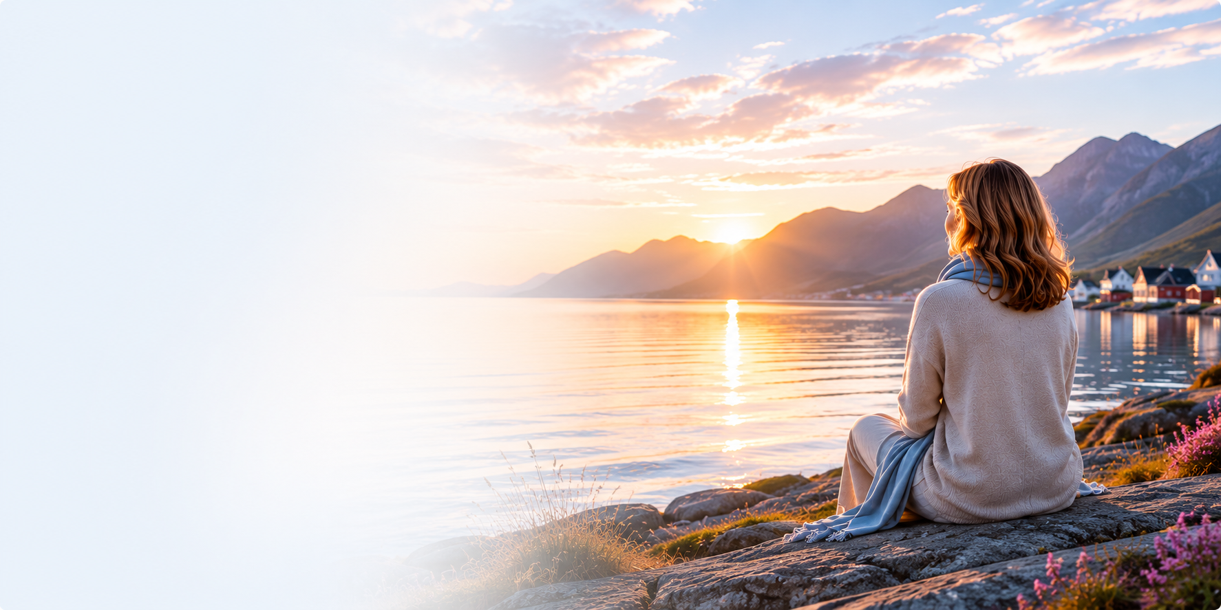A woman in a soft sweater sitting on coastal rocks at sunrise, watching the calm sea